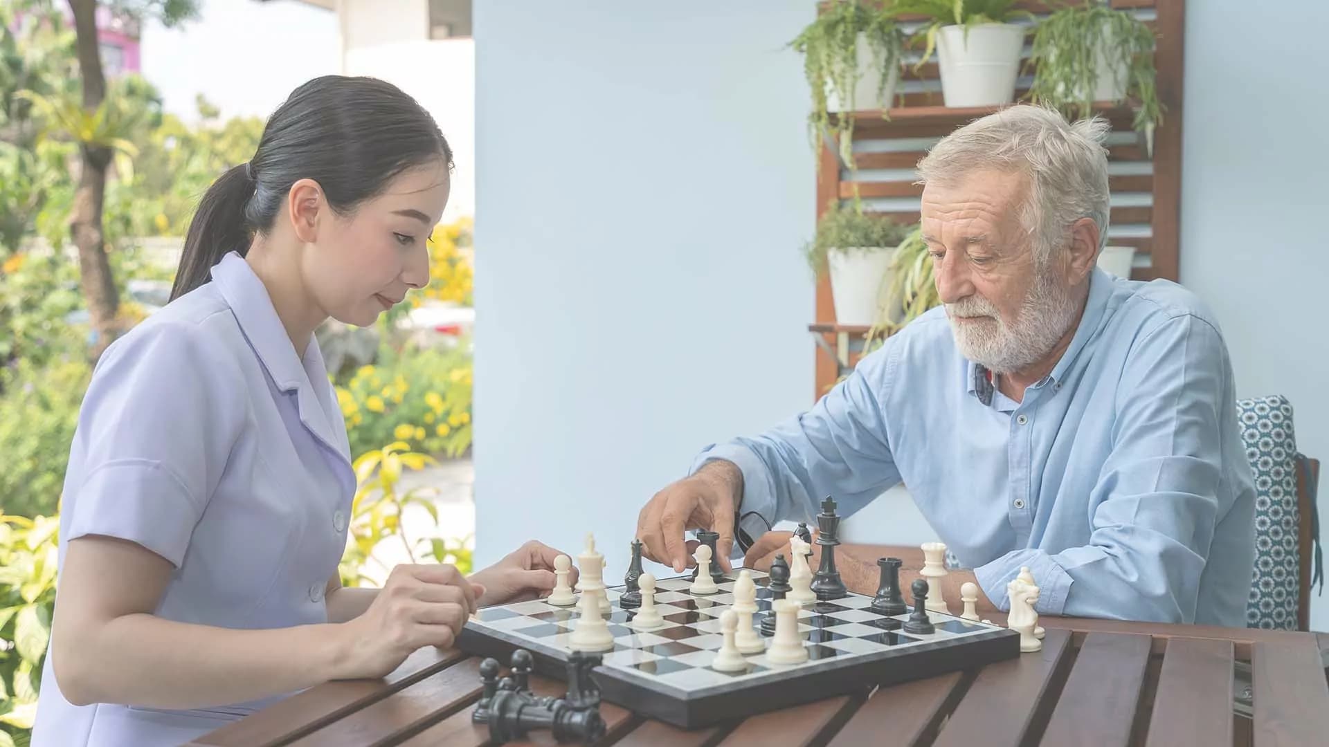 An older man playing chess outdoors with a caregiver