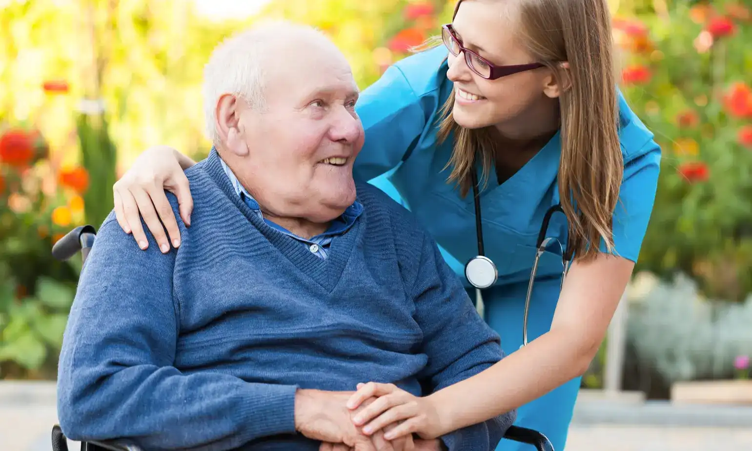A caregiver and an older man laughing together in a garden