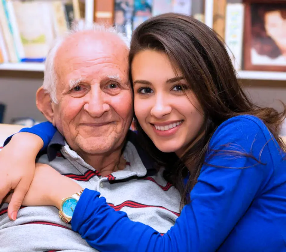 A granddaughter with her arm around her grandfather at home