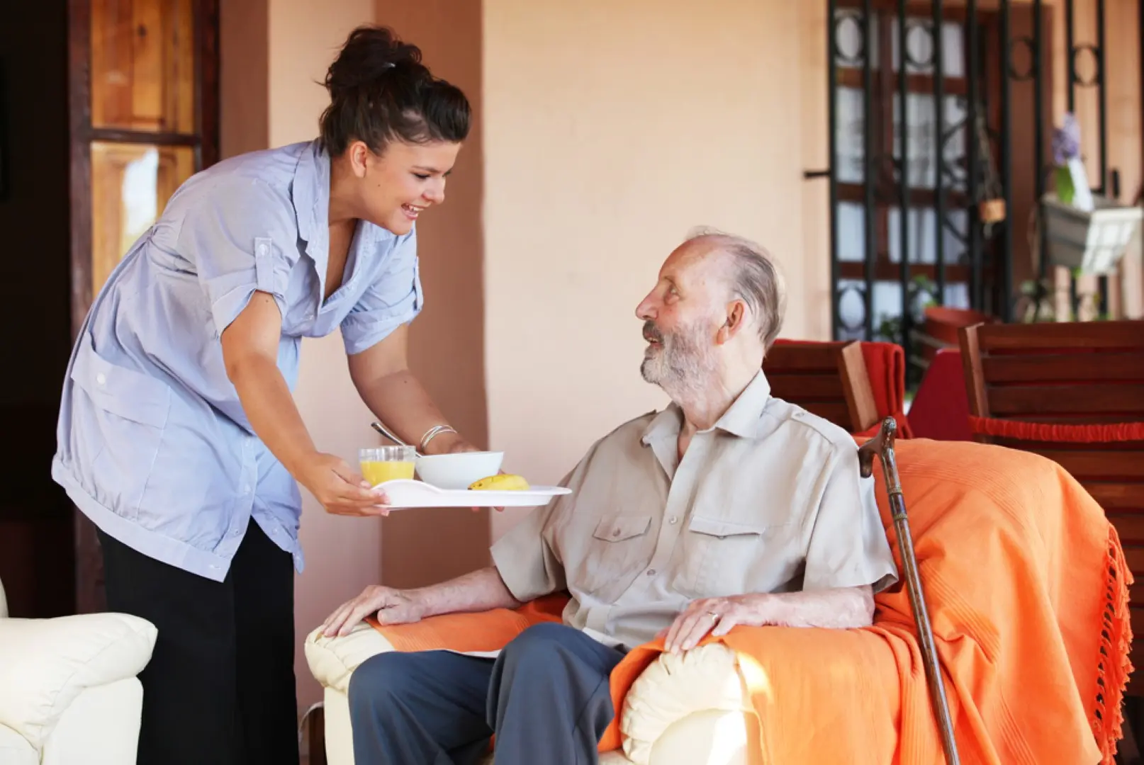 A caregiver serving a meal to an older man in his sitting room
