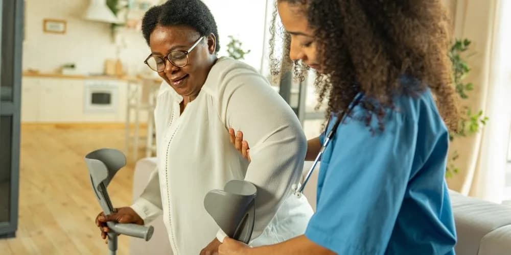 A caregiver steadying an older woman as she stands with a walking frame