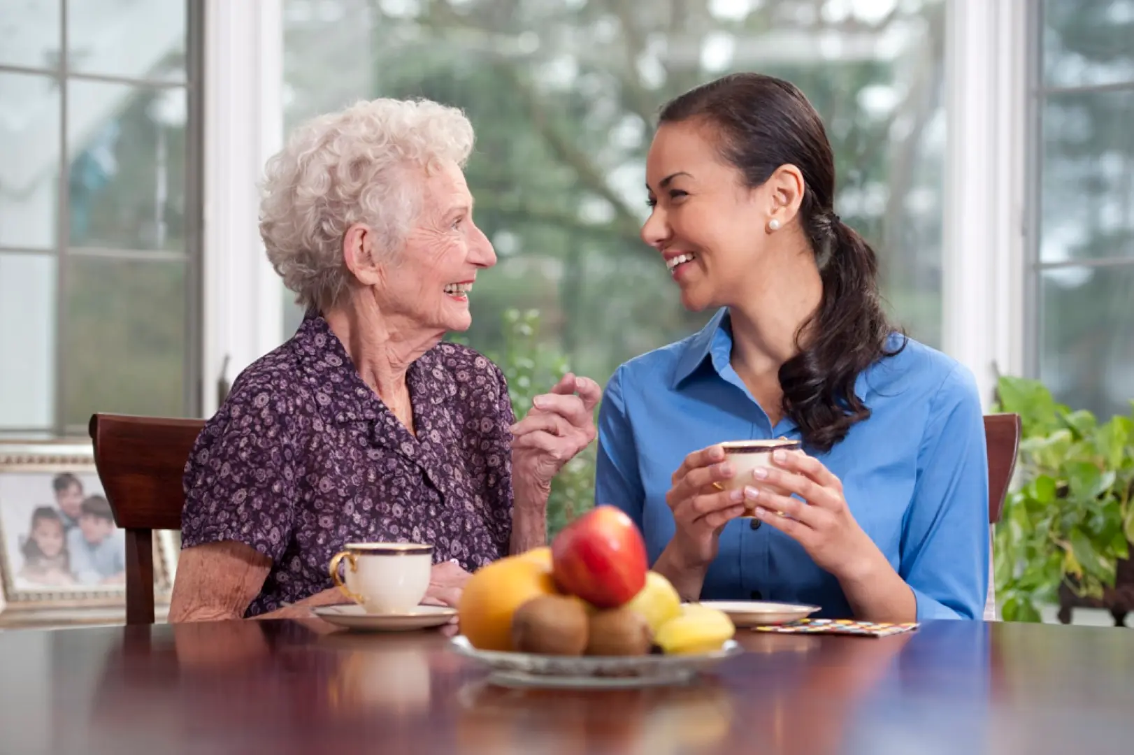 A caregiver and an older woman talking over coffee at her kitchen table